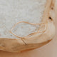 Gold bangle bracelet on a textured surface with a wooden bowl