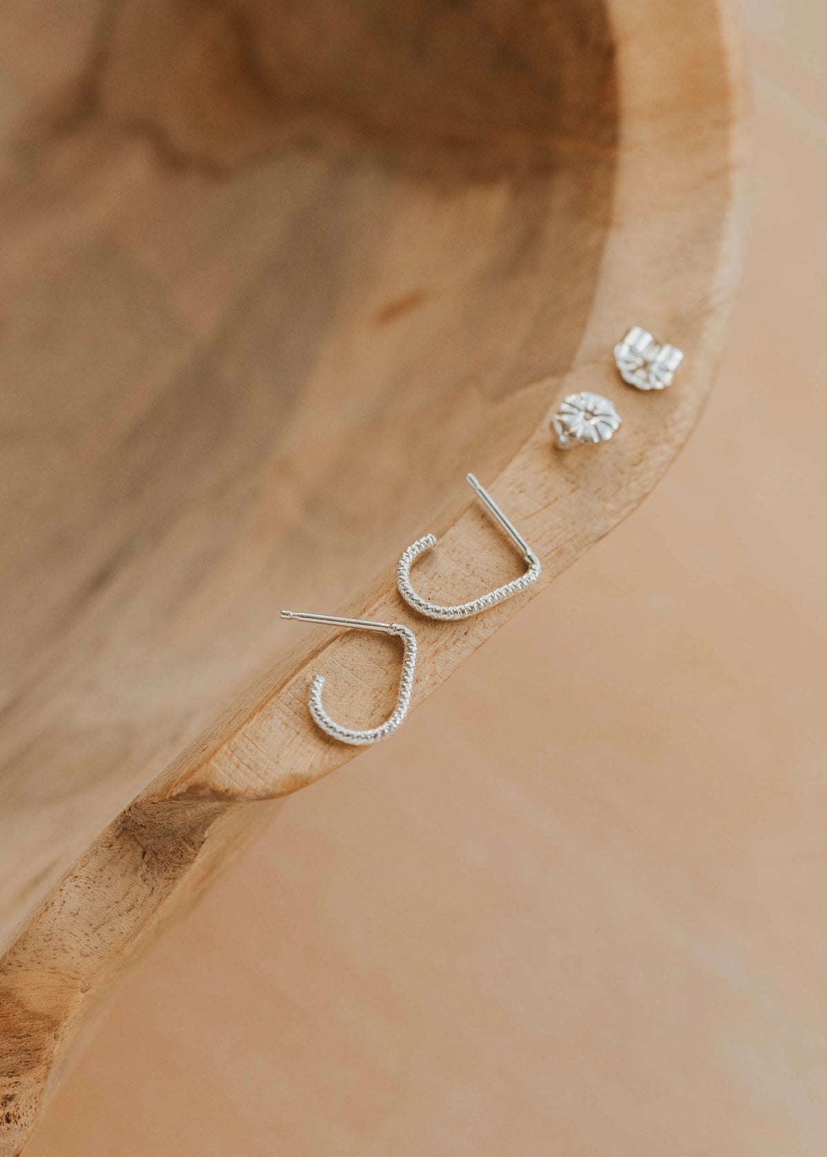 Silver earrings with 'J' design on a wooden surface