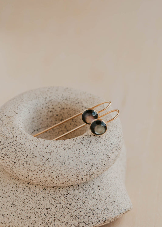 Pair of gold and black earrings on a textured stone surface with a soft beige background