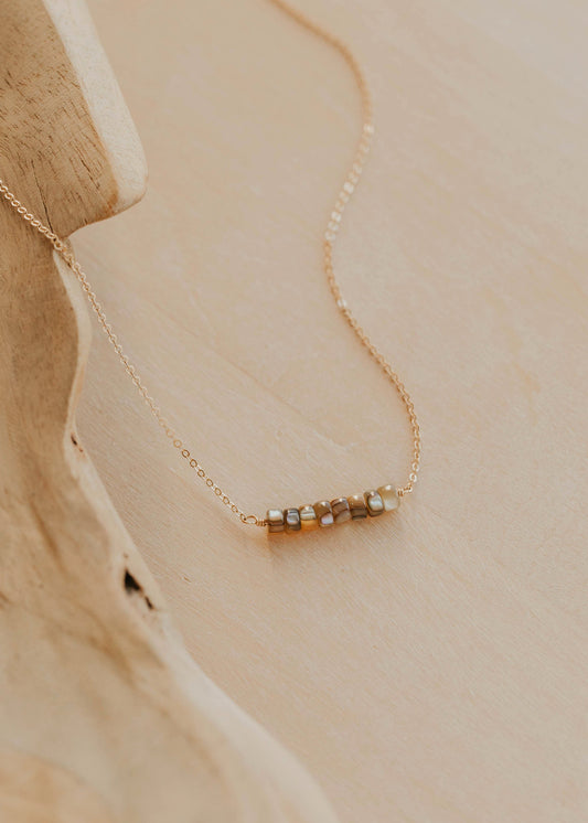 Delicate gold necklace with small beads on a beige stone surface