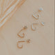 Set of gold and silver earrings on a beige surface with a leaf