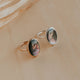Two gold rings with circular gemstones on a beige background