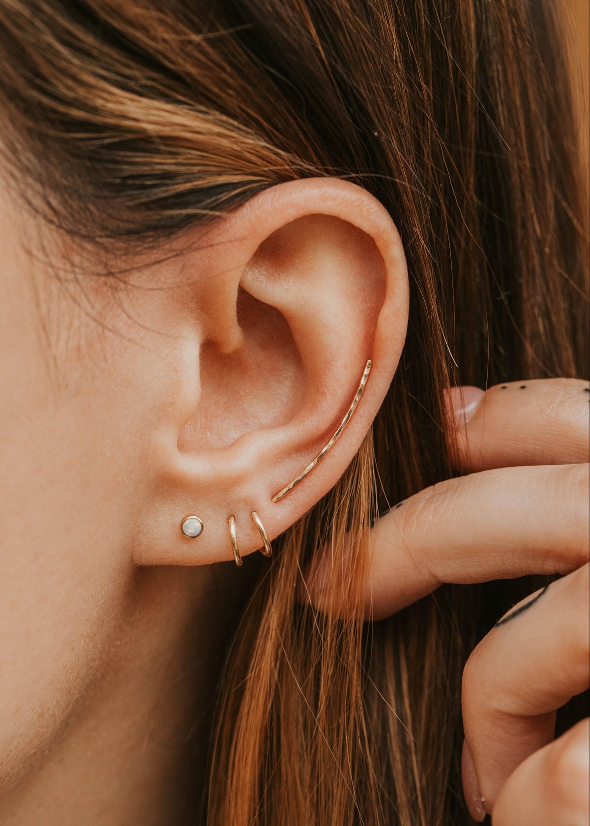 Close-up of an ear with gold earrings and hair being adjusted.