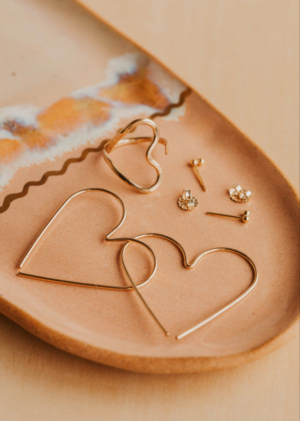 Gold heart-shaped earrings on a beige ceramic dish