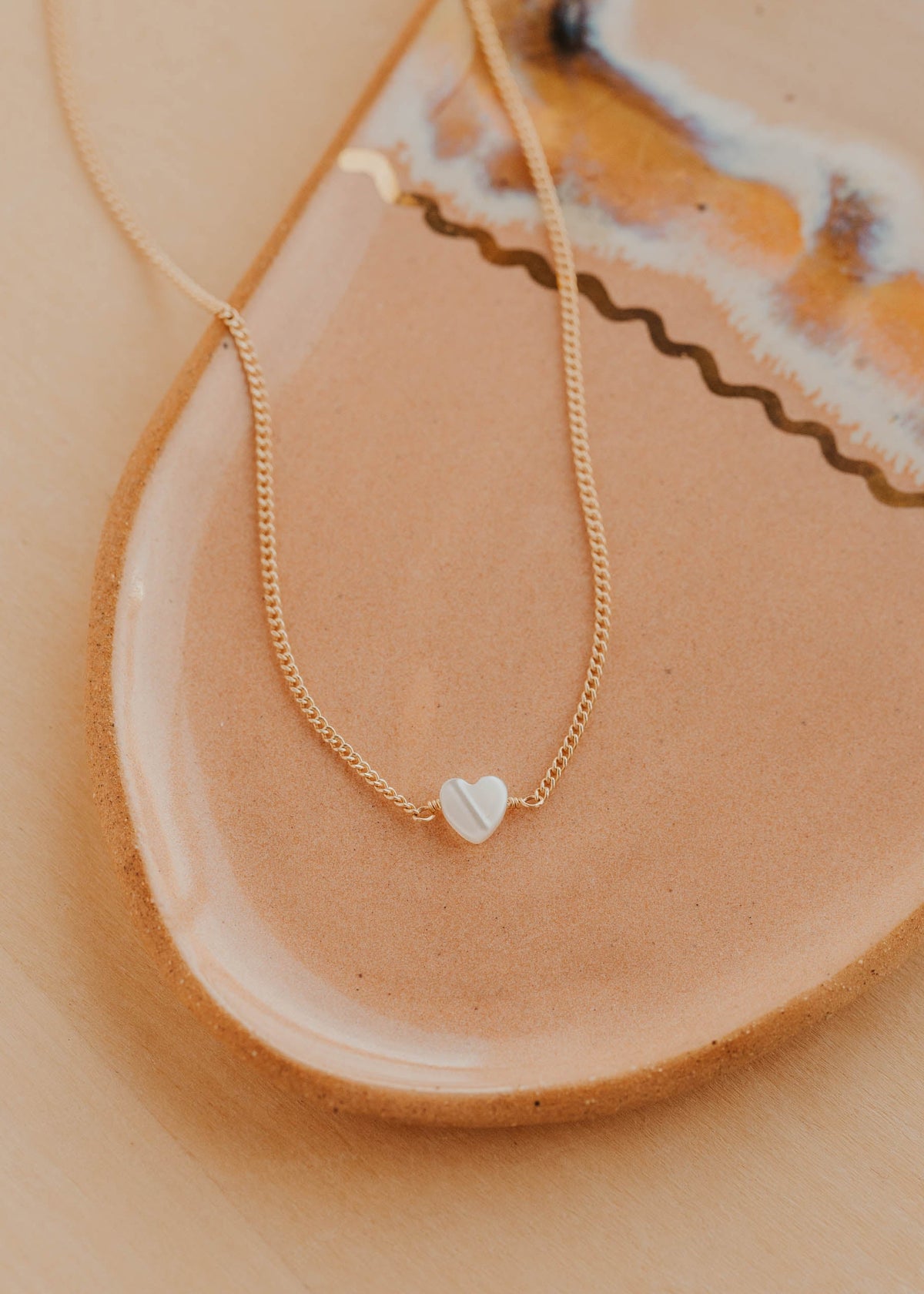 Gold necklace with a heart pendant on a ceramic plate