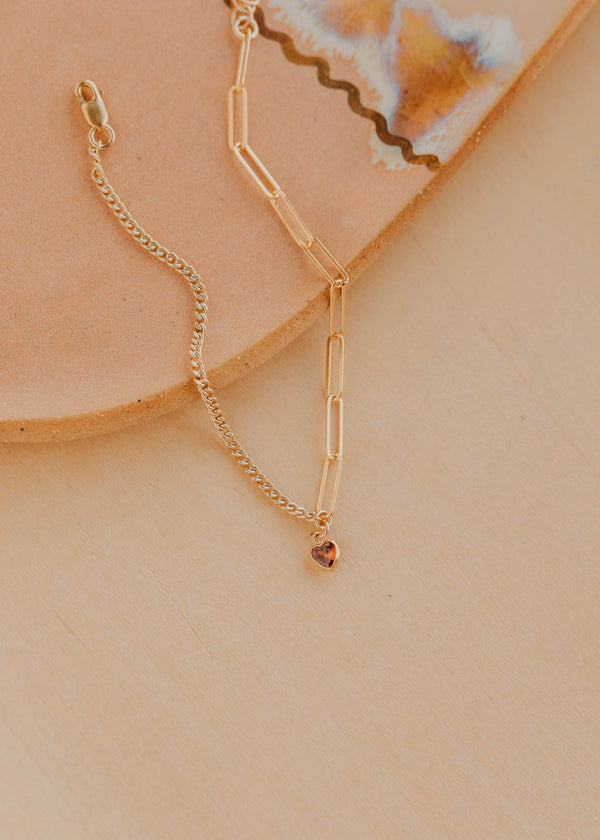 Gold bracelet with a small pendant on a beige surface