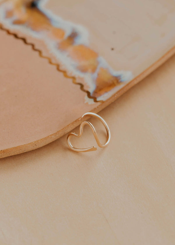 Gold heart-shaped ring on a beige surface with a blurred background