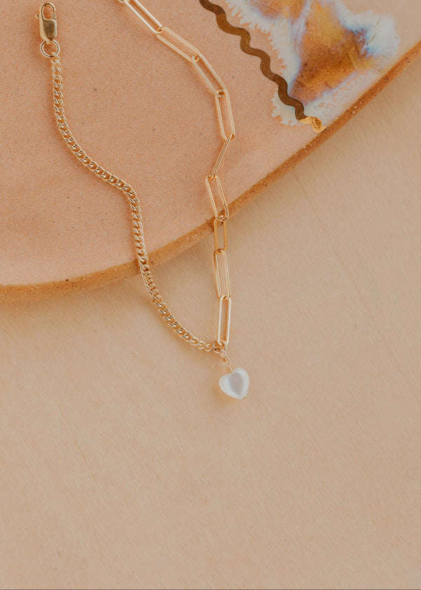 Gold chain bracelet with a heart pendant on a beige surface