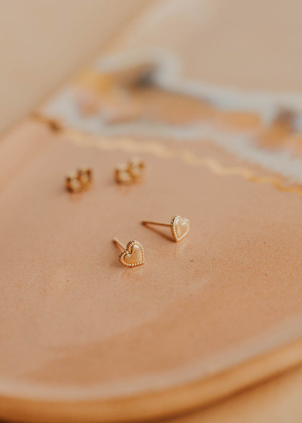 Gold heart-shaped earrings on a beige surface