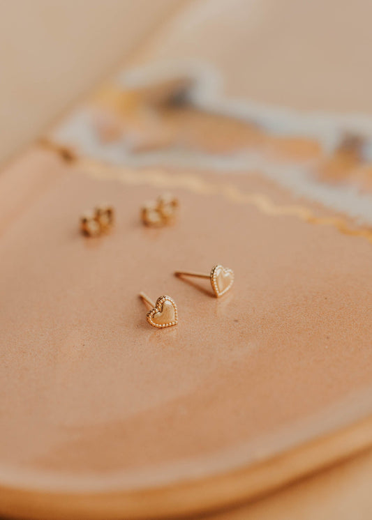 Gold heart-shaped earrings on a beige surface