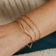 Close-up of a person's wrist wearing gold bracelets on a neutral background