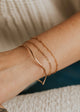 Close-up of a person's wrist wearing gold bracelets on a neutral background