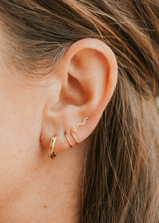 Close-up of an ear wearing gold hoop earrings with a blurred background