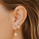 Close-up of an ear with gold earrings and an opal, with blurred hair in the background