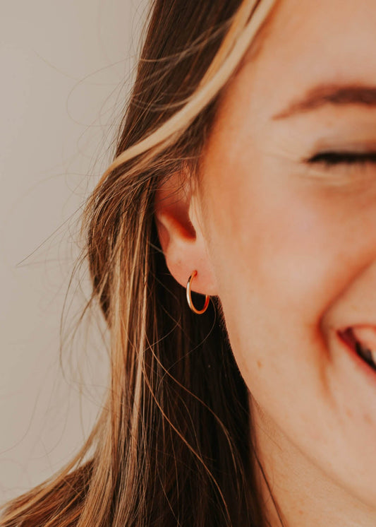 Small gold hoop earring by Hello Adorn shown styled in a model's ear in an infinity hoops style.