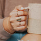 A gold ring stack shown on a model wearing a wrap ring to look like 2 rings, a Supermoon Ring as the statement ring to look like a moon ring, a thin band, a thin hammered ring, and a braided ring styled by Hello Adorn shown in 14k gold fill.
