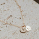 Gold stamped jewelry attached to a gold initial necklace by Hello Adorn laying flat.