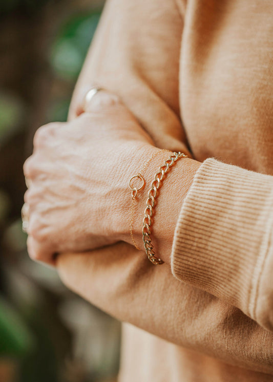 A bracelet stack with a thick gold bracelet and a chain linked bracelet with interlocking circles in Tiny Links Bracelet, both in a chain bracelet style by Hello Adorn.